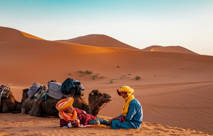 man in yellow robe sitting on brown sand during daytime