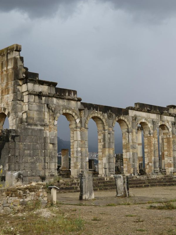 Ancient Roman ruins of Volubilis in Morocco, showcasing stone arches and dramatic cloudy sky.